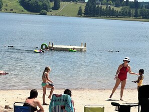 A lakeside scene with people in swimwear, a dock, and a grassy area.