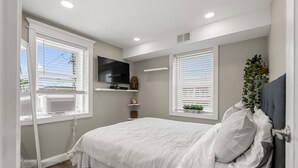 Un dormitorio con cama, televisor y dos ventanas con persianas.