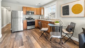 Una cocina moderna con electrodomésticos de acero inoxidable, armarios de madera y un comedor con mesa de vidrio y sillas metálicas.