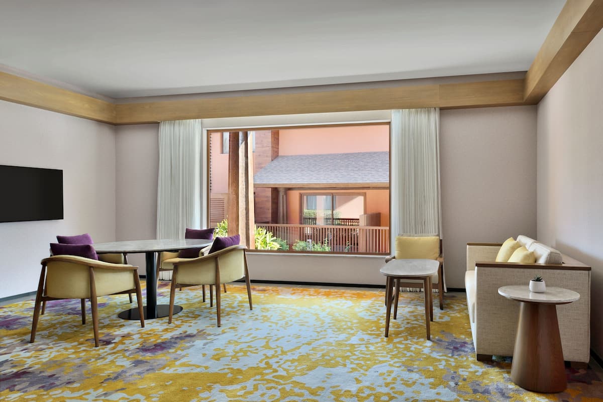 Una habitación de hotel con balcón, zona de comedor con sillas y mesa, y un sofá.