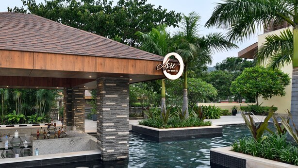 A pool area with a wooden roof structure, stone pillars, and a sign that reads "Asu the pool bar".