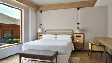 Habitación de hotel con una cama grande, un escritorio y un banco. Una ventana ofrece vistas al exterior.
