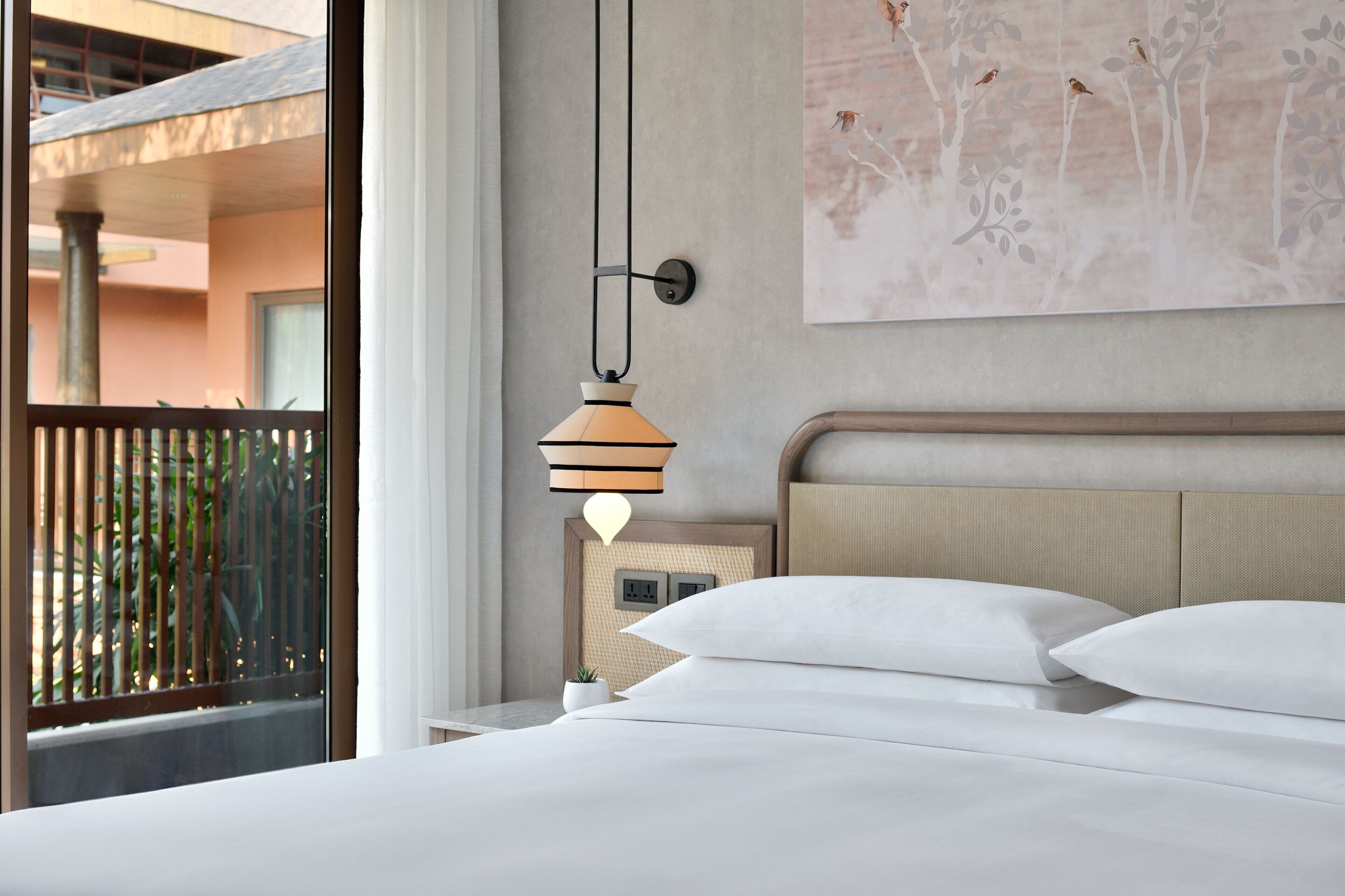 Een hotelkamer met een bed, een wandlamp en uitzicht op het balkon.