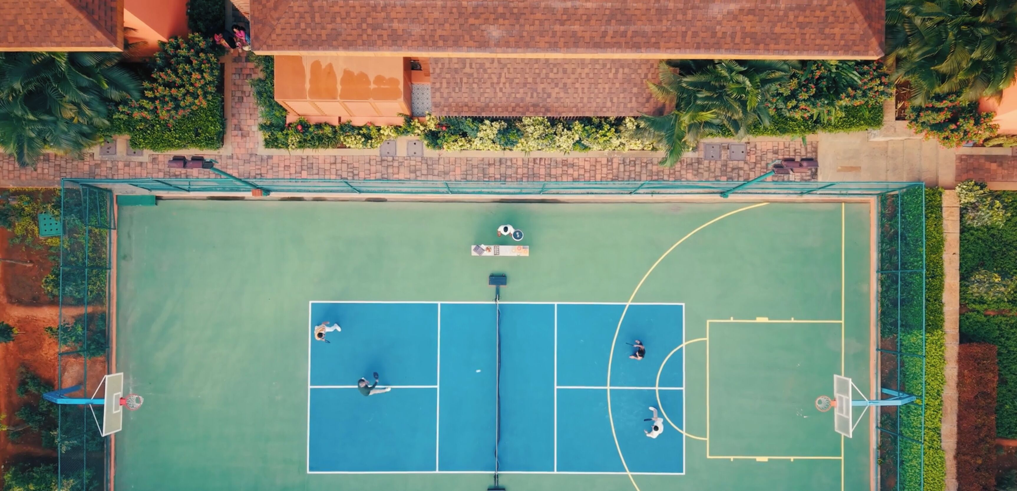 Vista aérea de una cancha de tenis con follaje circundante y un edificio.