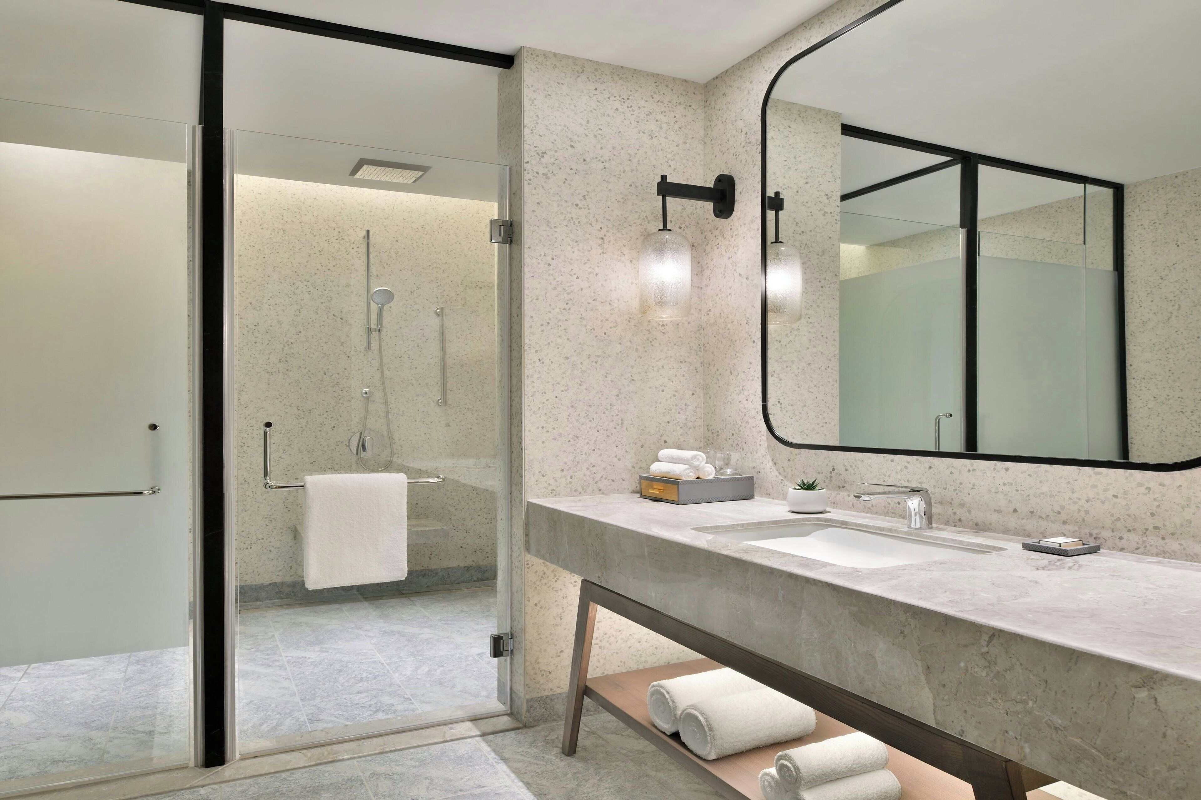 A modern bathroom with a glass-enclosed shower, a large mirror, and a marble countertop.