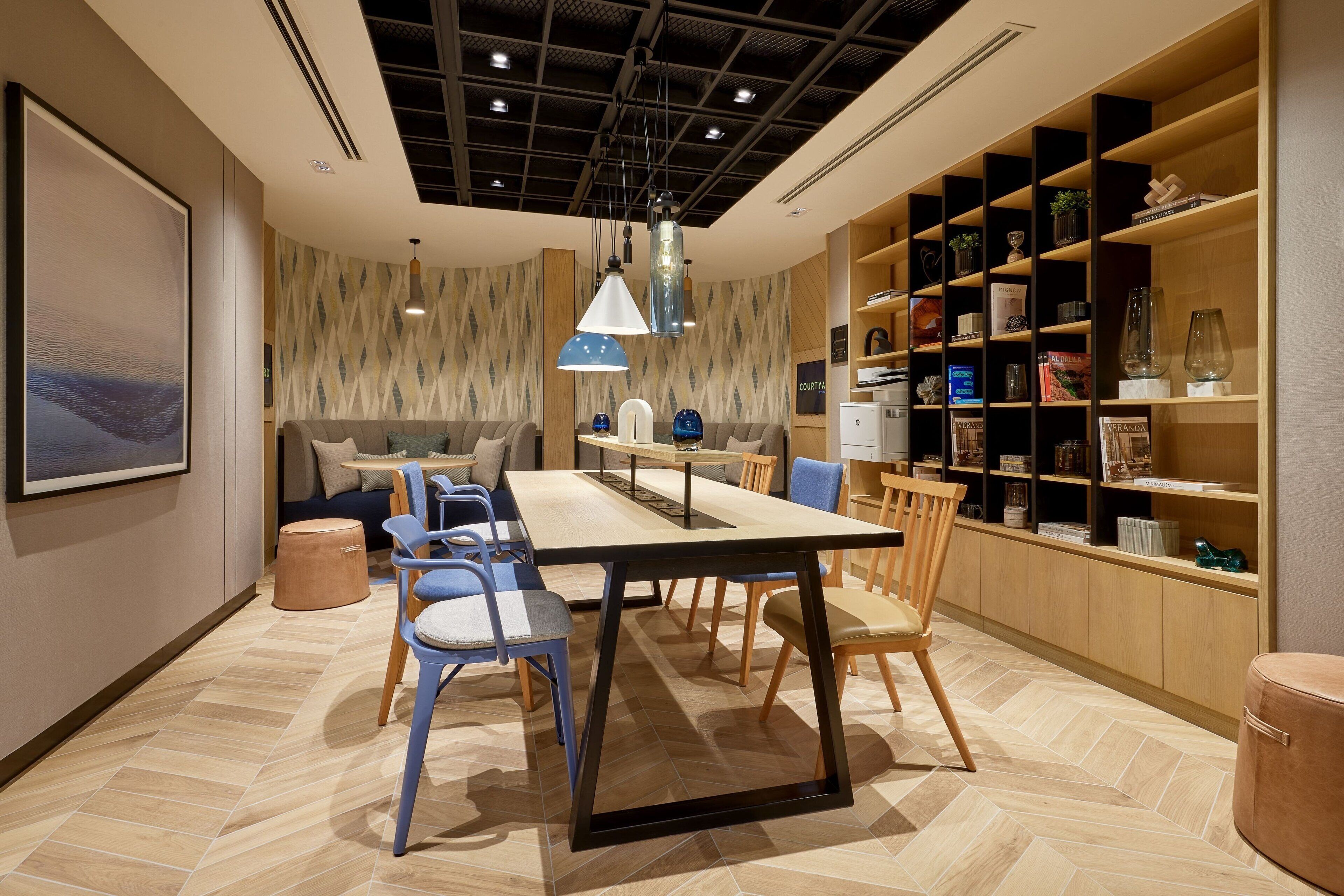 A modern dining area with a long table, chairs, and a bookshelf.