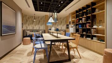A modern dining area with a long table, chairs, and a bookshelf.