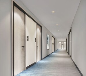A long, narrow hallway with doors marked with numbers, a carpeted floor, and recessed ceiling lighting. - Courtyard By Marriott Jubail (Al Jubail)