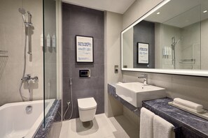 A modern bathroom with a glass-enclosed shower, a standalone toilet, a large mirror, and a marble countertop. - Courtyard By Marriott Jubail (Al Jubail)