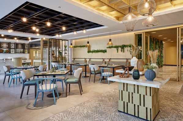Un restaurante moderno con varias mesas y sillas, iluminación colgante y plantas decorativas.