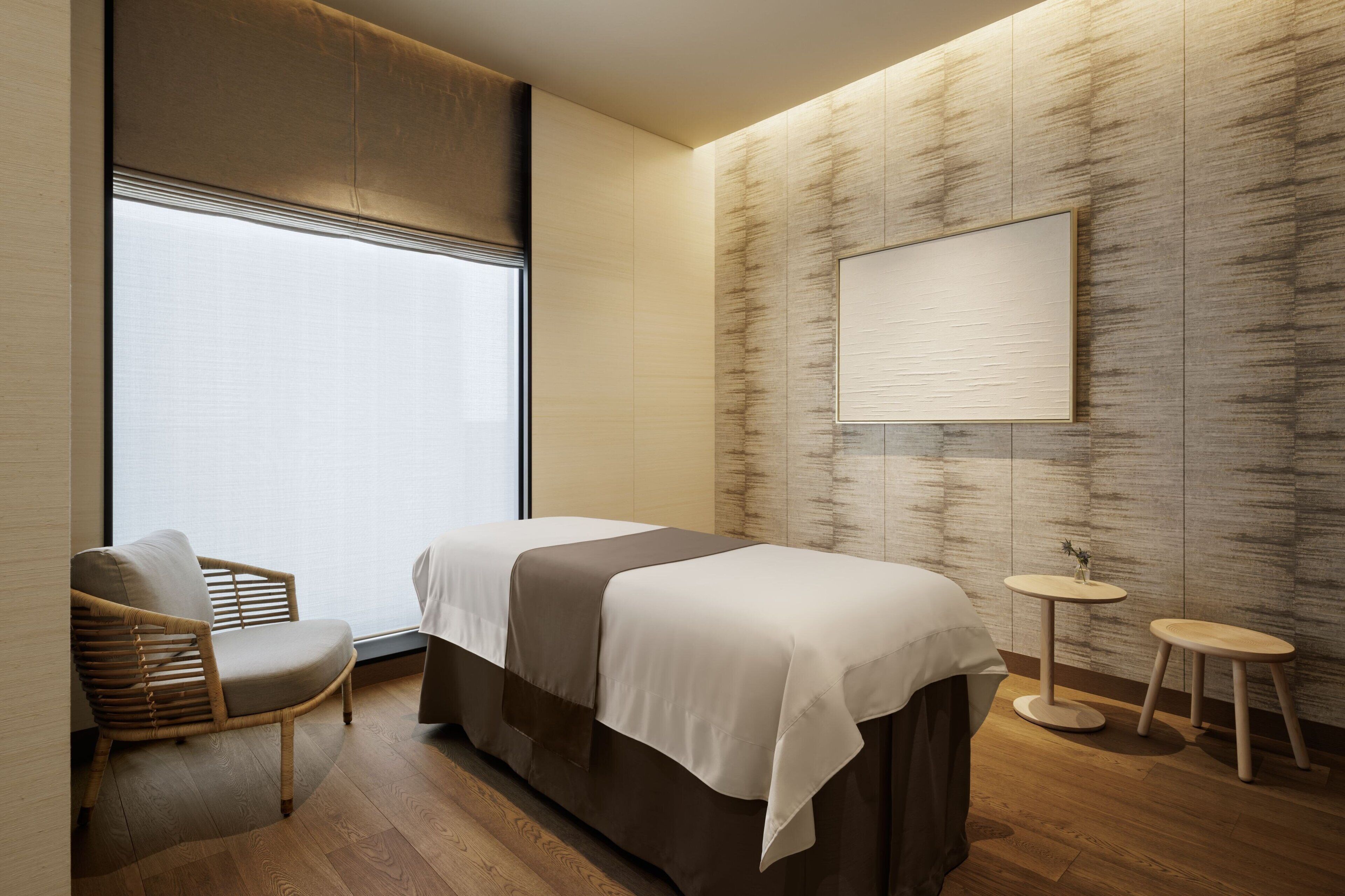 A modern hotel room with a bed, a chair, two small tables, and a large window.