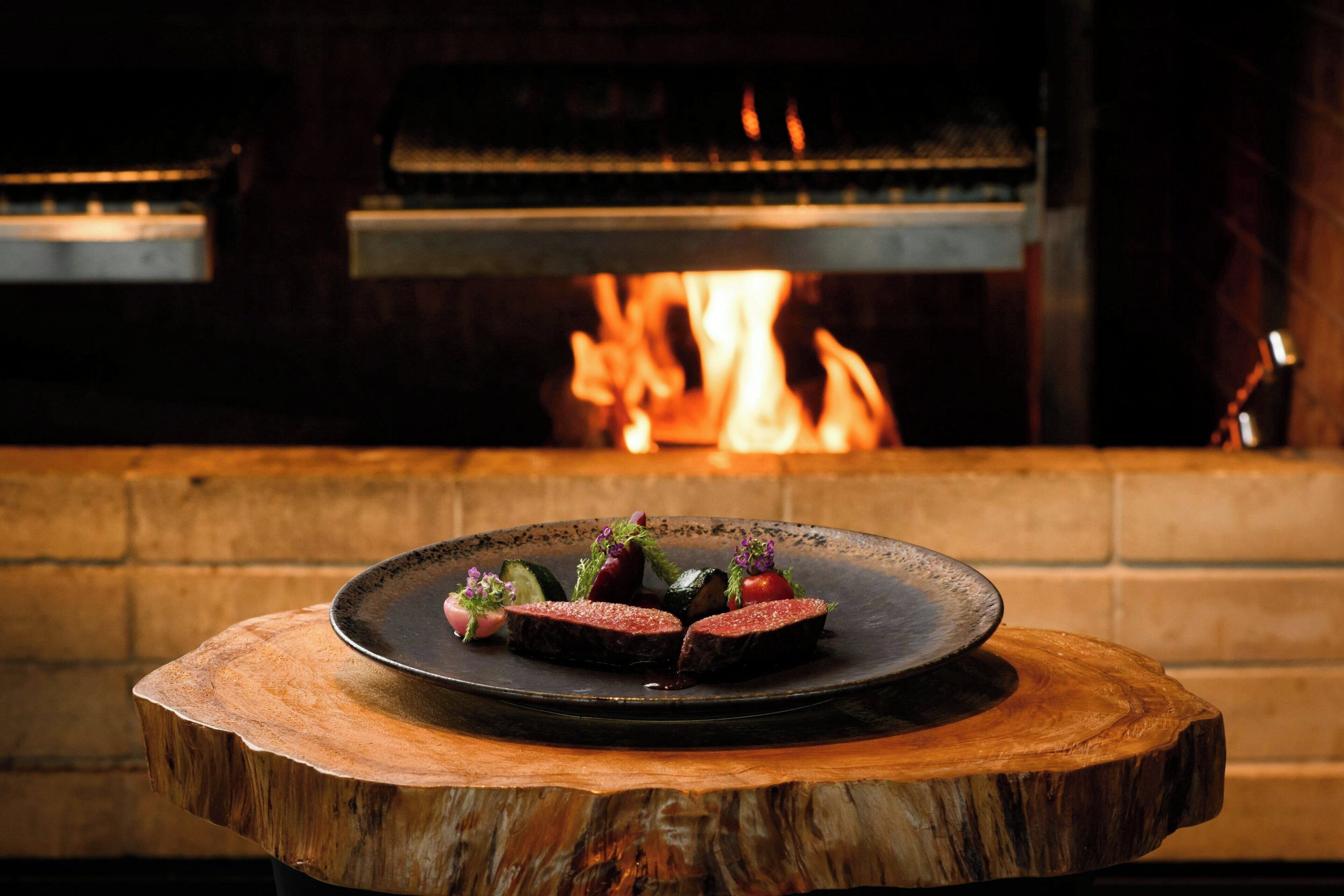 A wooden table with a plate of food in front of a fireplace.