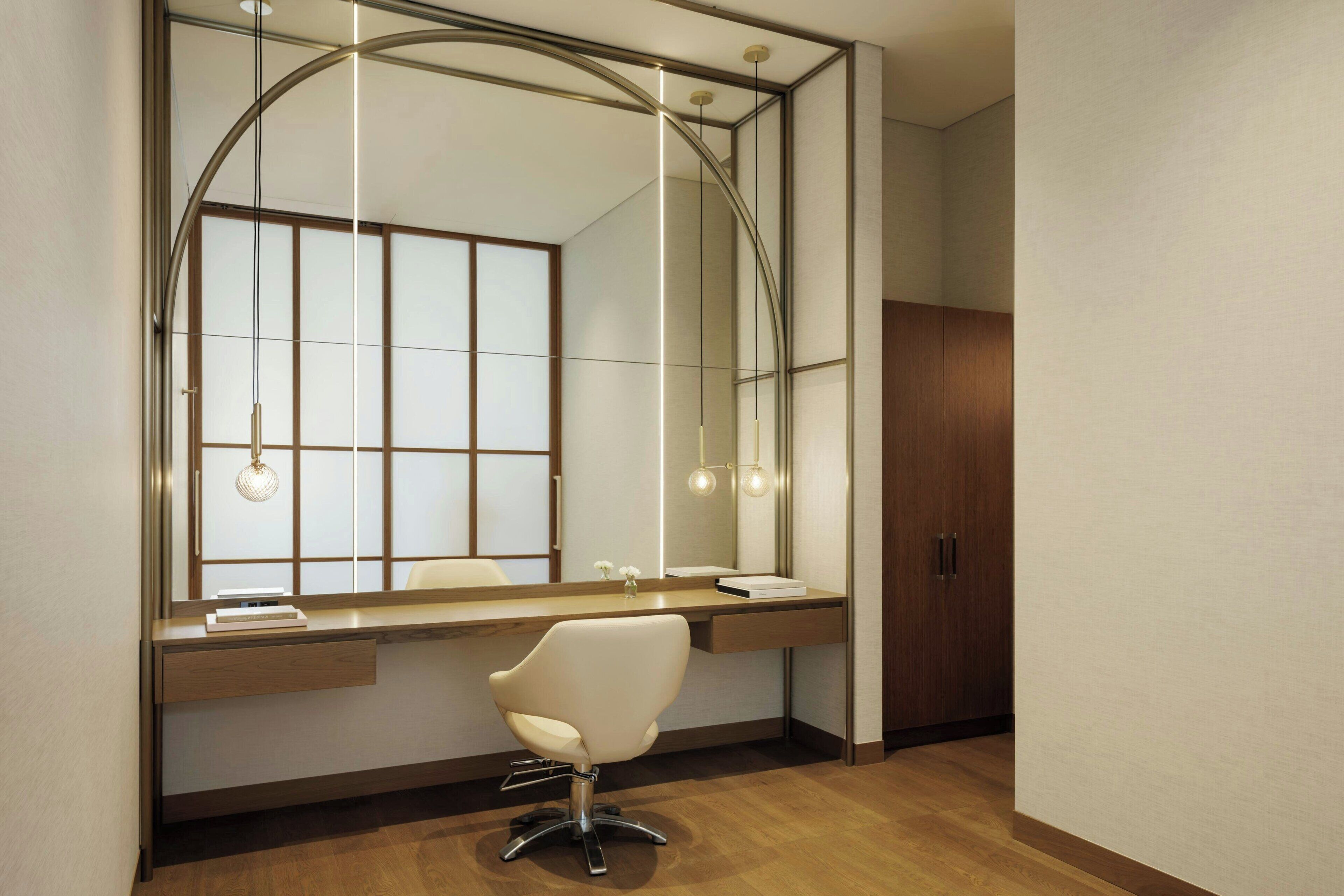 A modern bathroom with a large mirror, wooden vanity, and a white chair.