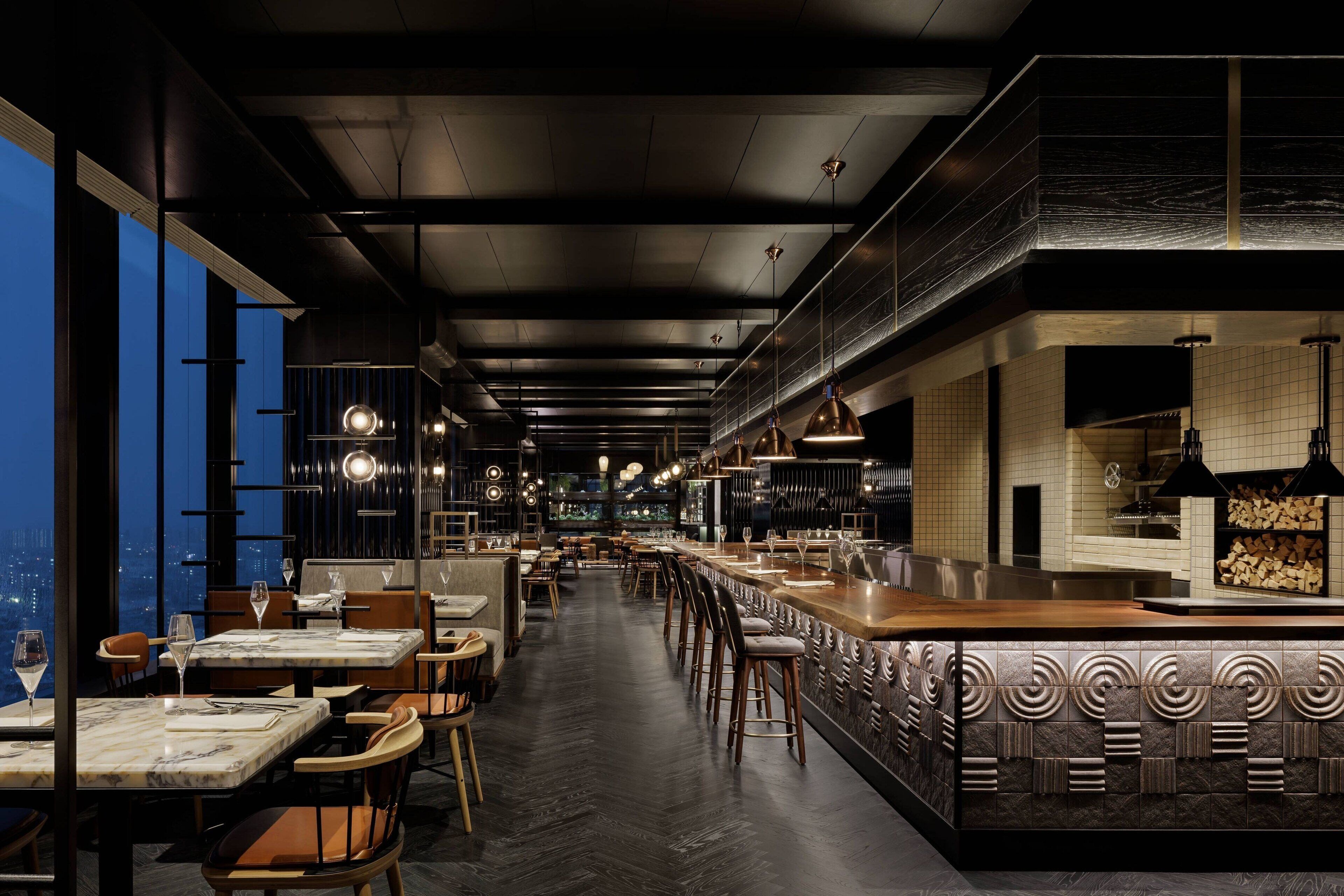 A modern restaurant with a long counter, high ceilings, and large windows overlooking a cityscape.
