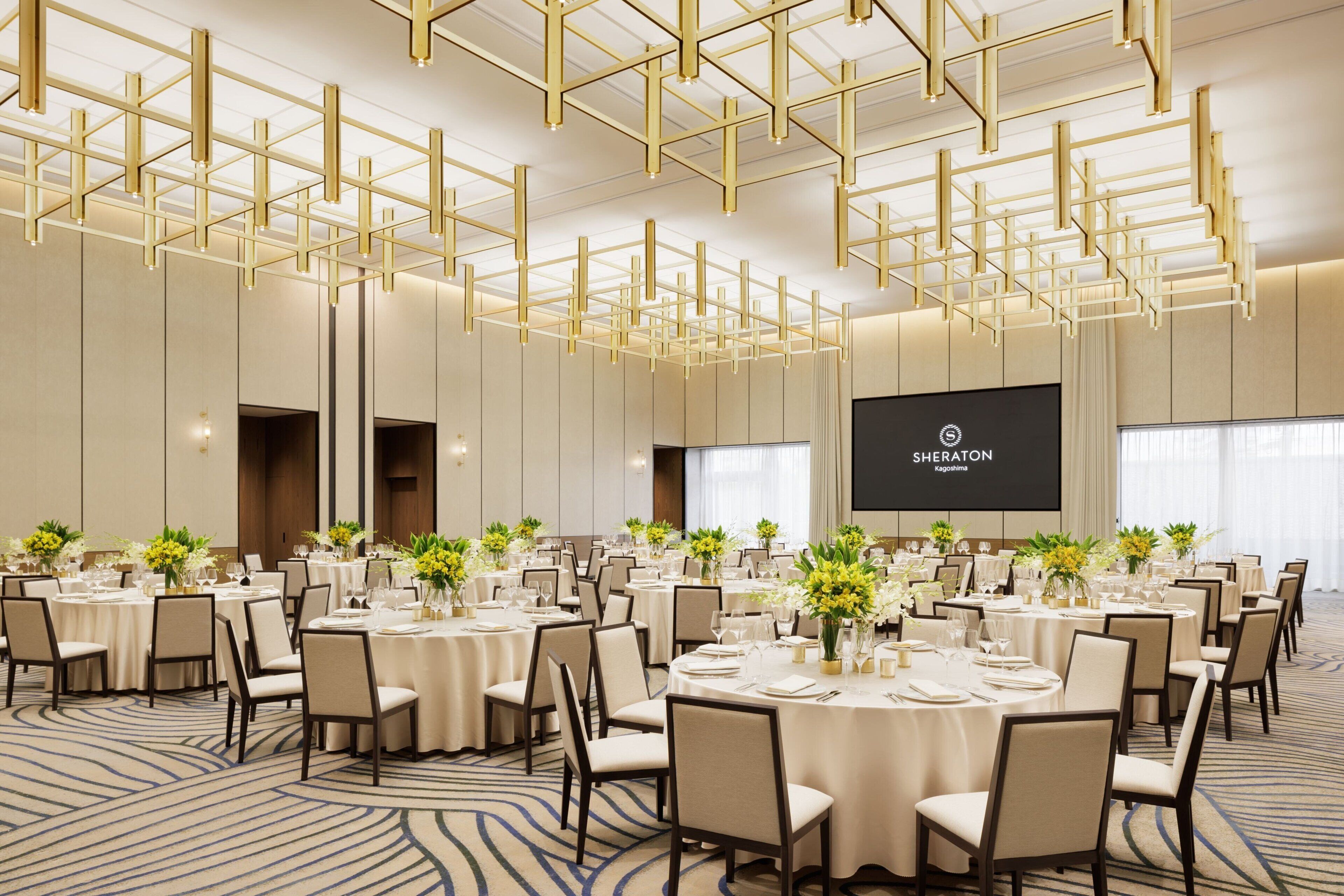 A conference room with round tables, chairs, and a large screen displaying 'Sheraton'.