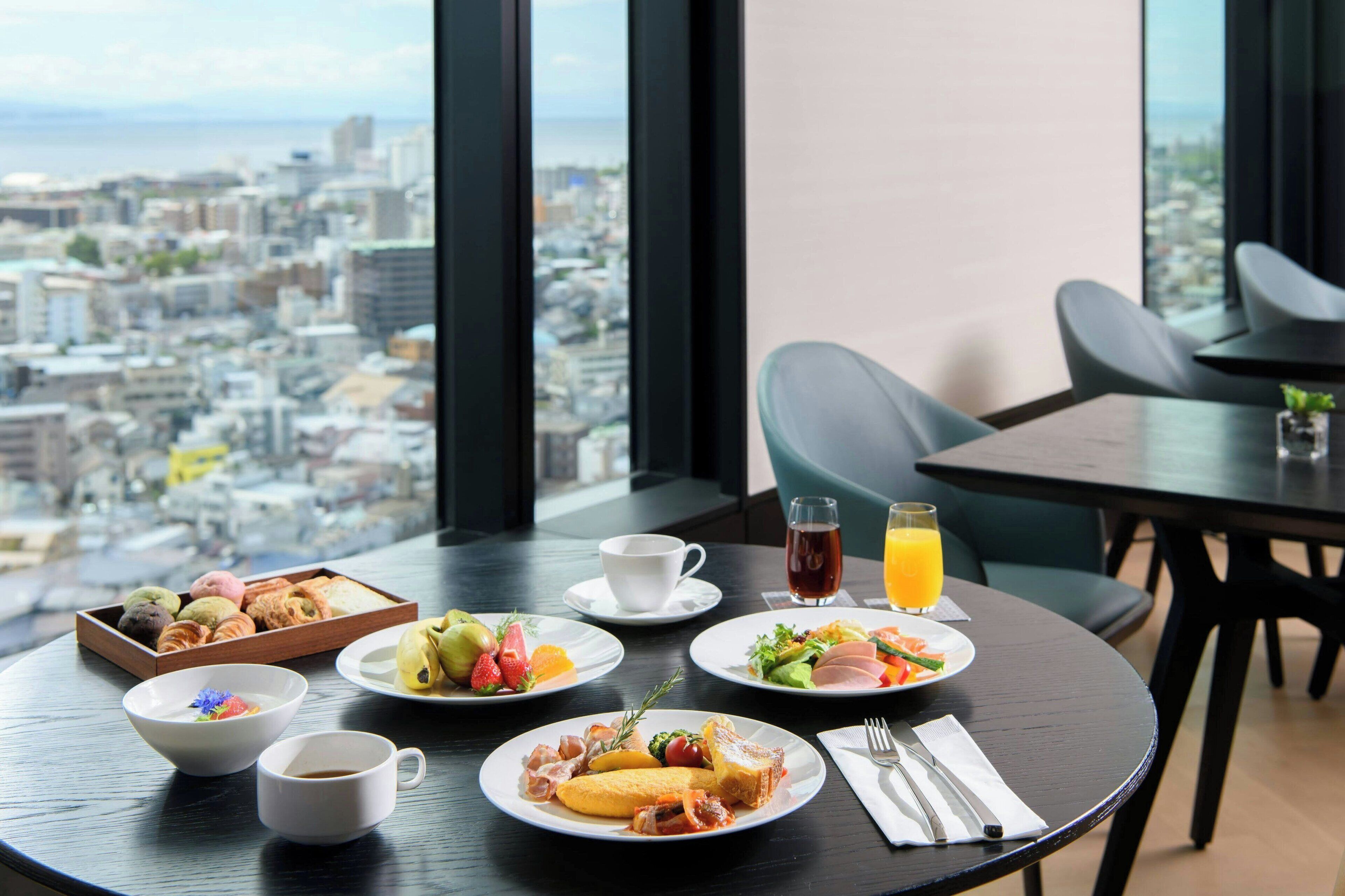 A dining table with breakfast items, a city view, and modern furniture.