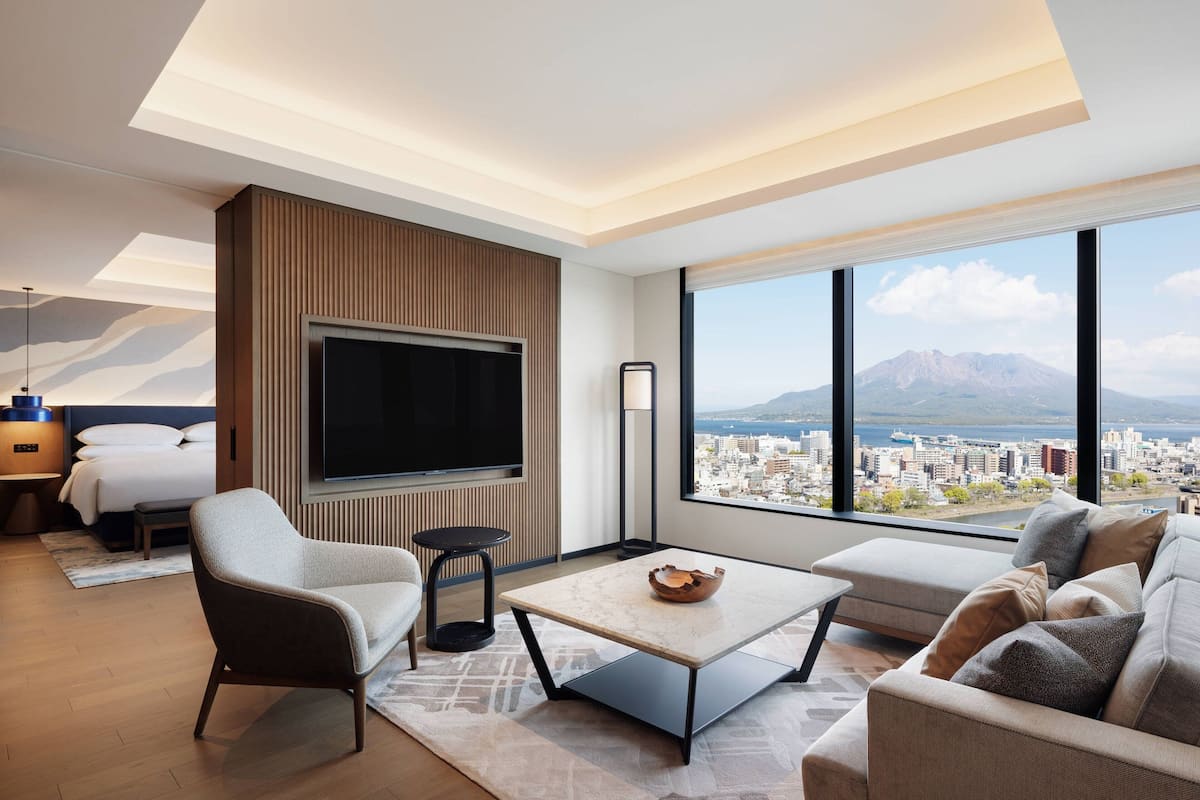 Ein modernes Hotelzimmer mit großem Fernseher, gemütlicher Sitzecke, kleinem Tisch und Blick auf die Stadt.