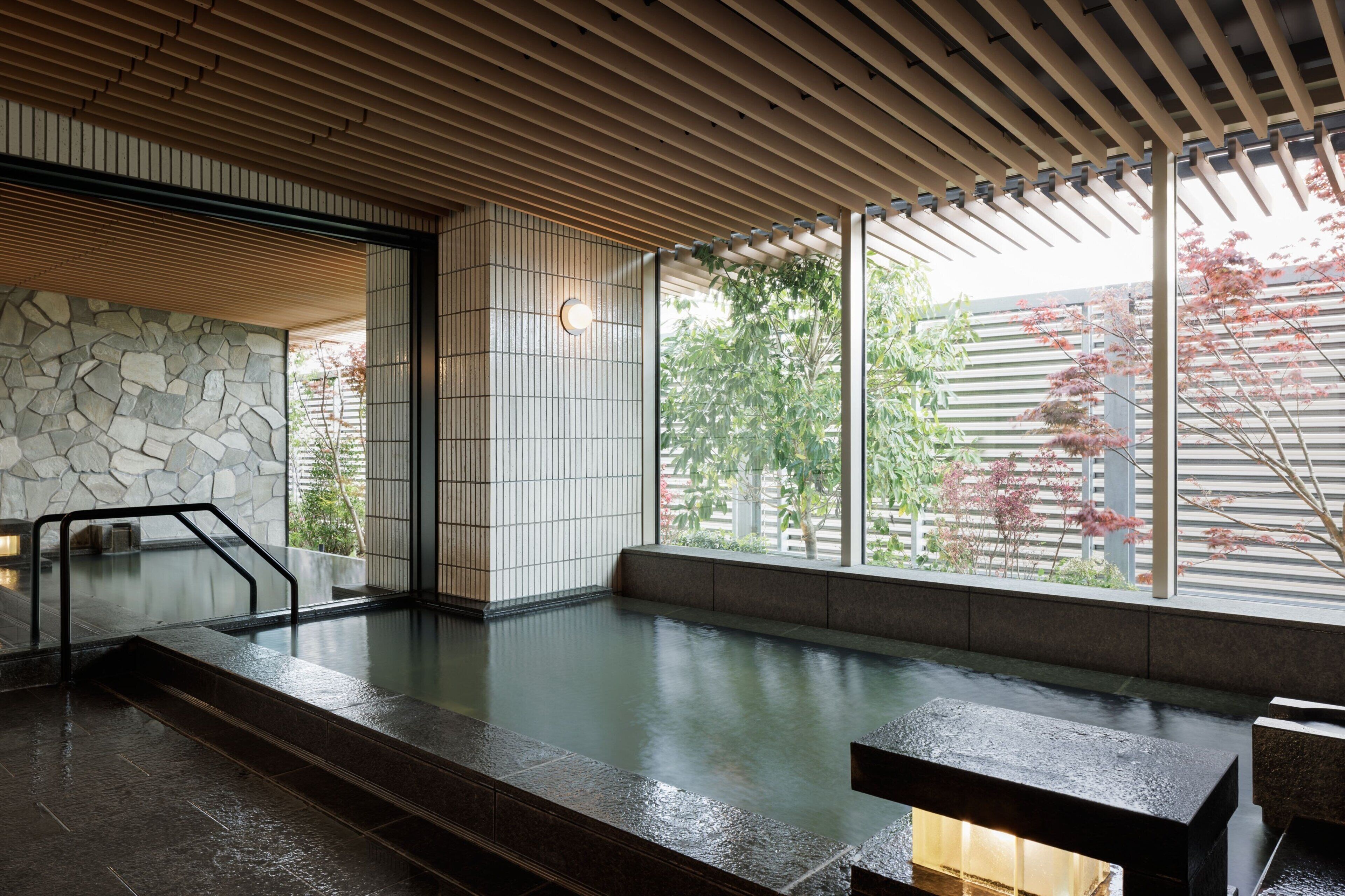 Un onsen japonés tradicional con pared de piedra, techo de madera y vistas a los cerezos en flor.