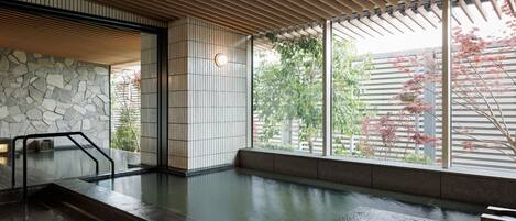 Un onsen japonés tradicional con pared de piedra, techo de madera y vistas a los cerezos en flor.