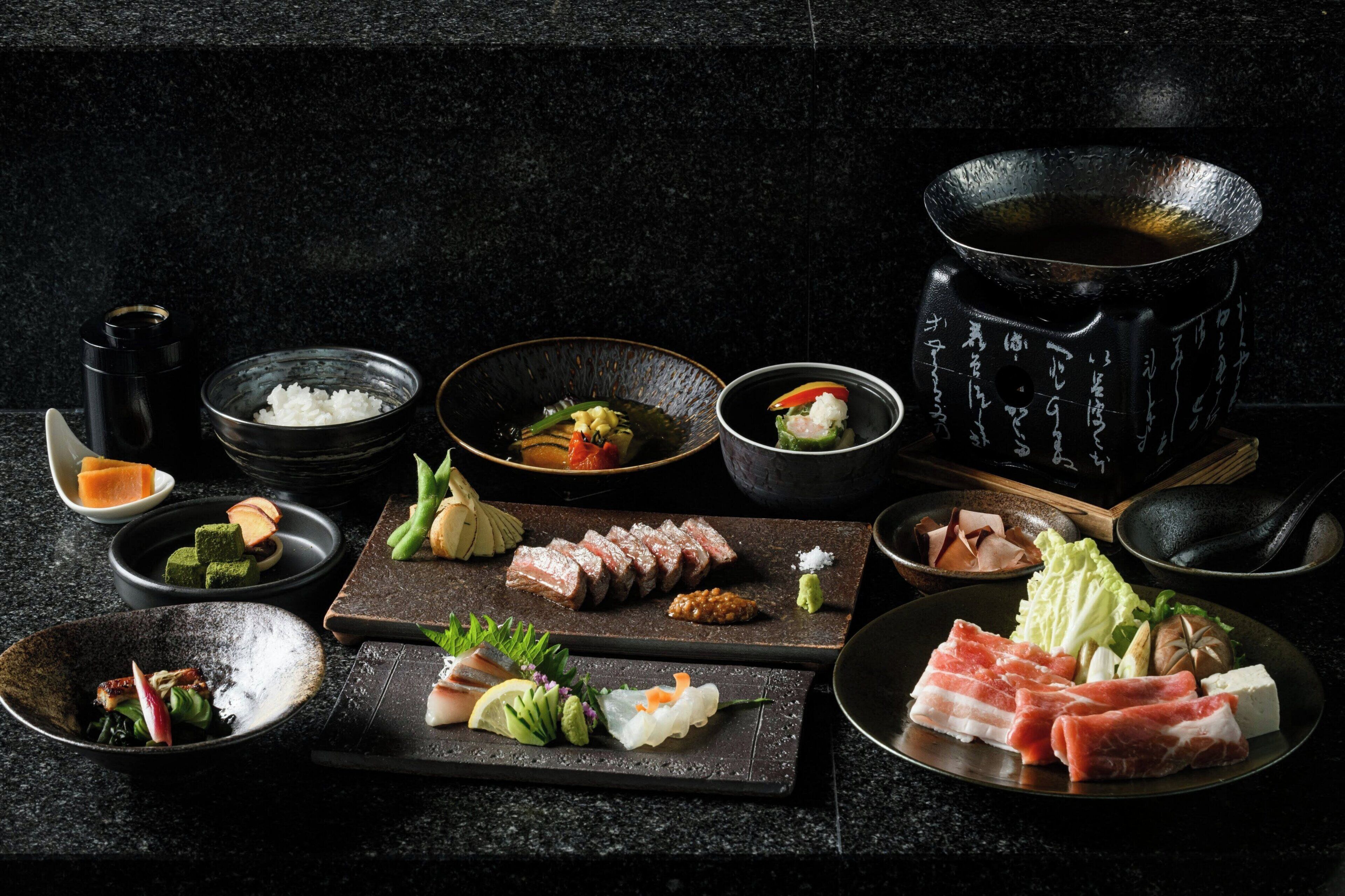 A variety of Japanese dishes and a teapot on a dark countertop.