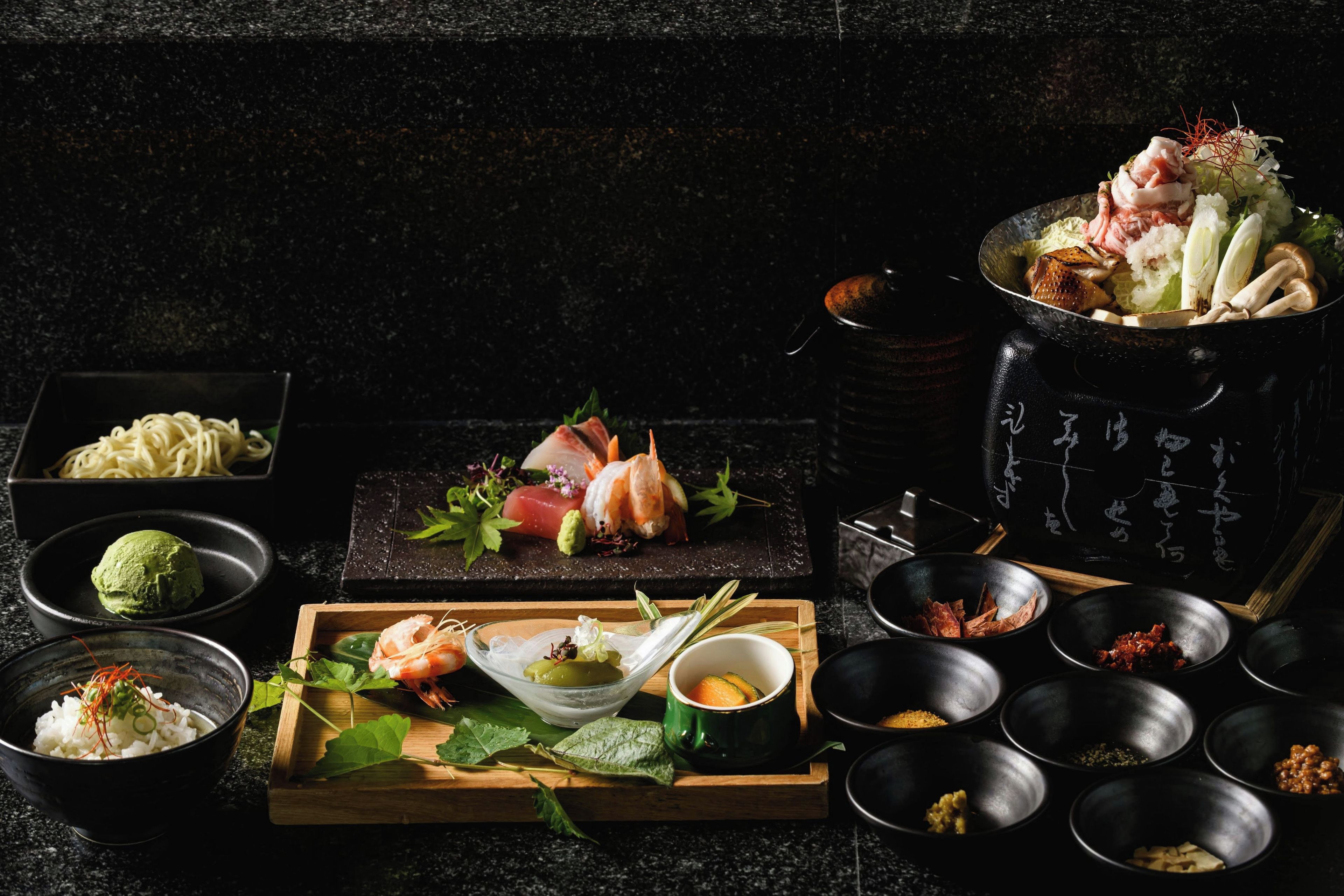 Forskellige japanske retter, herunder sushi, sashimi og tempura, anrettet på en mørk bordplade.