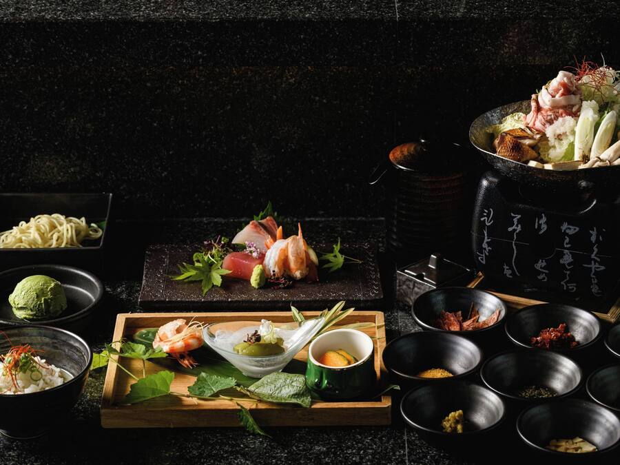 Forskellige japanske retter, herunder sushi, sashimi og tempura, anrettet på en mørk bordplade.