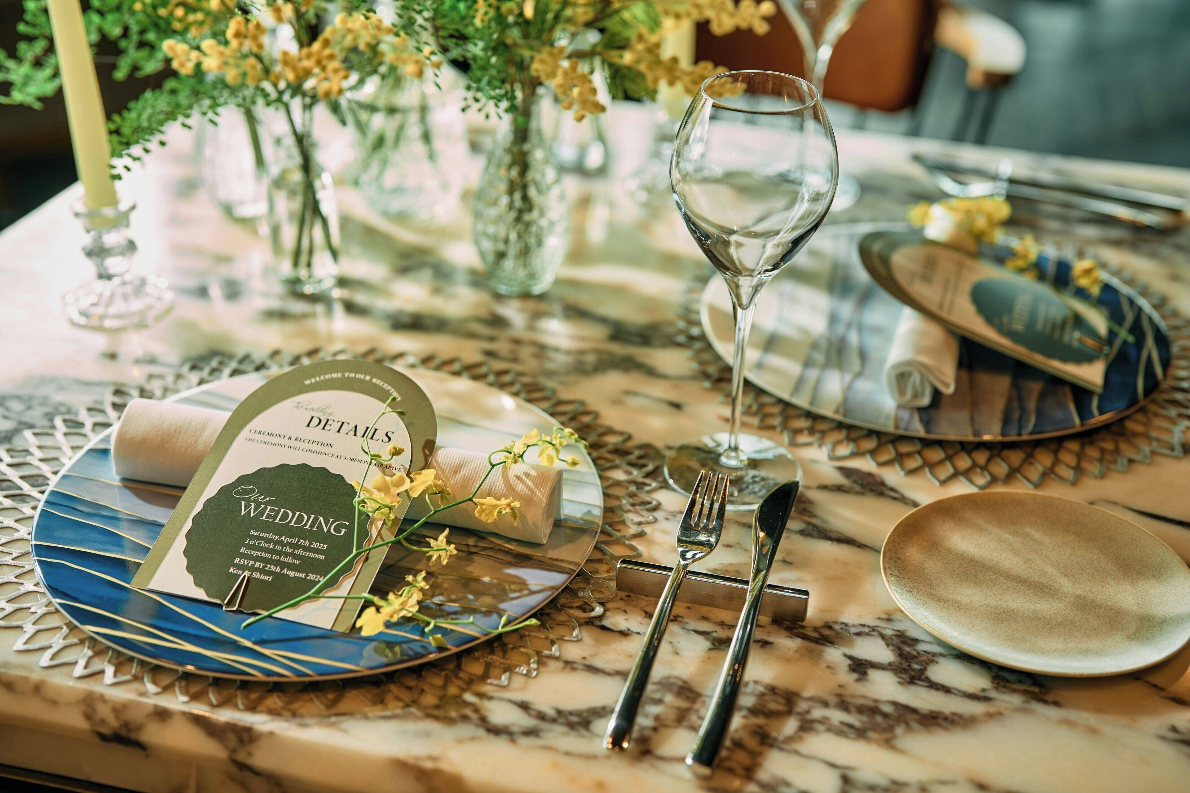 A table set for a wedding reception with a wedding card, glassware, and cutlery.