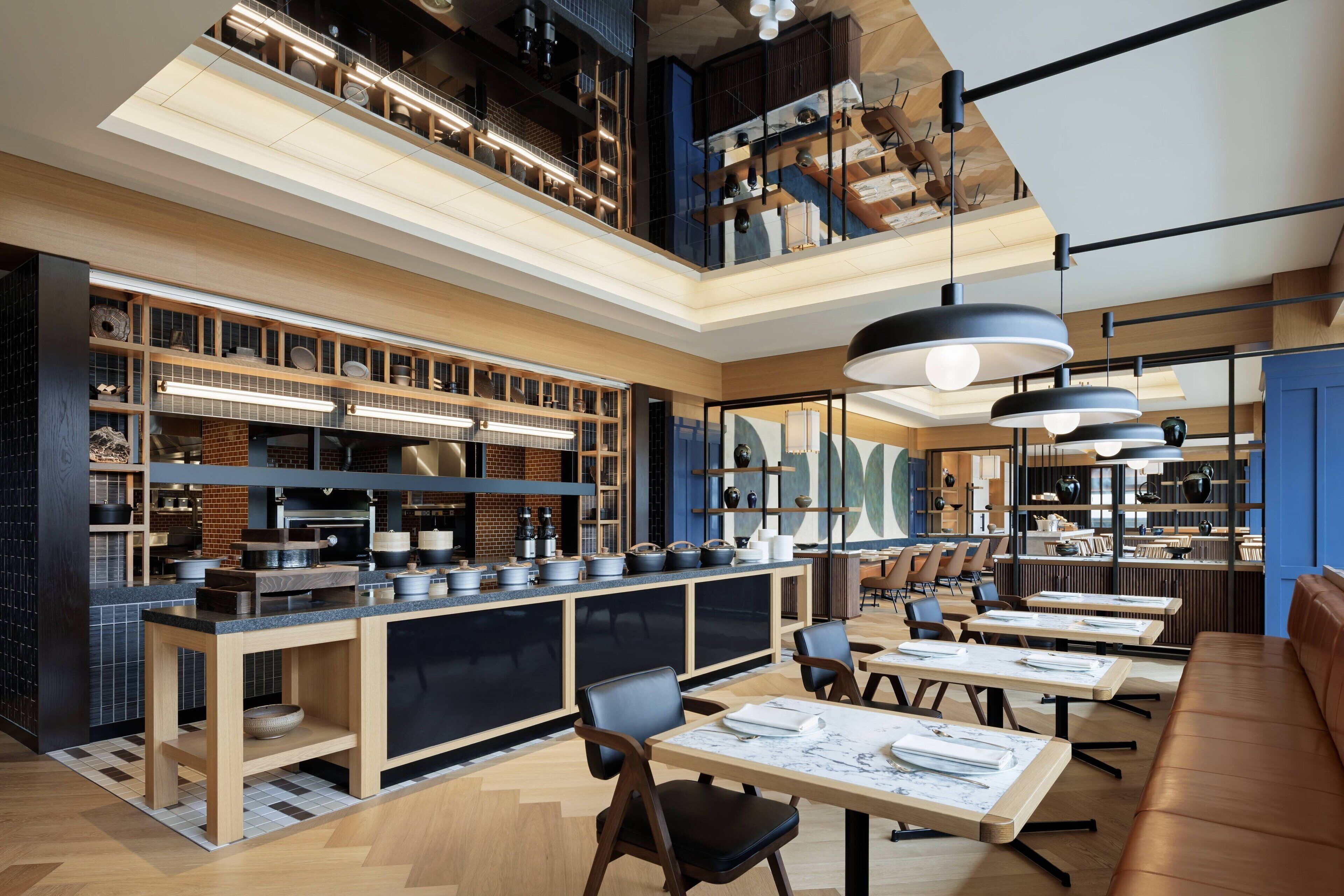Un restaurante moderno con mostrador central, zona de mesas y techos altos con vigas a la vista.
