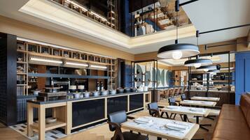 Un restaurante moderno con mostrador central, zona de mesas y techos altos con vigas a la vista.