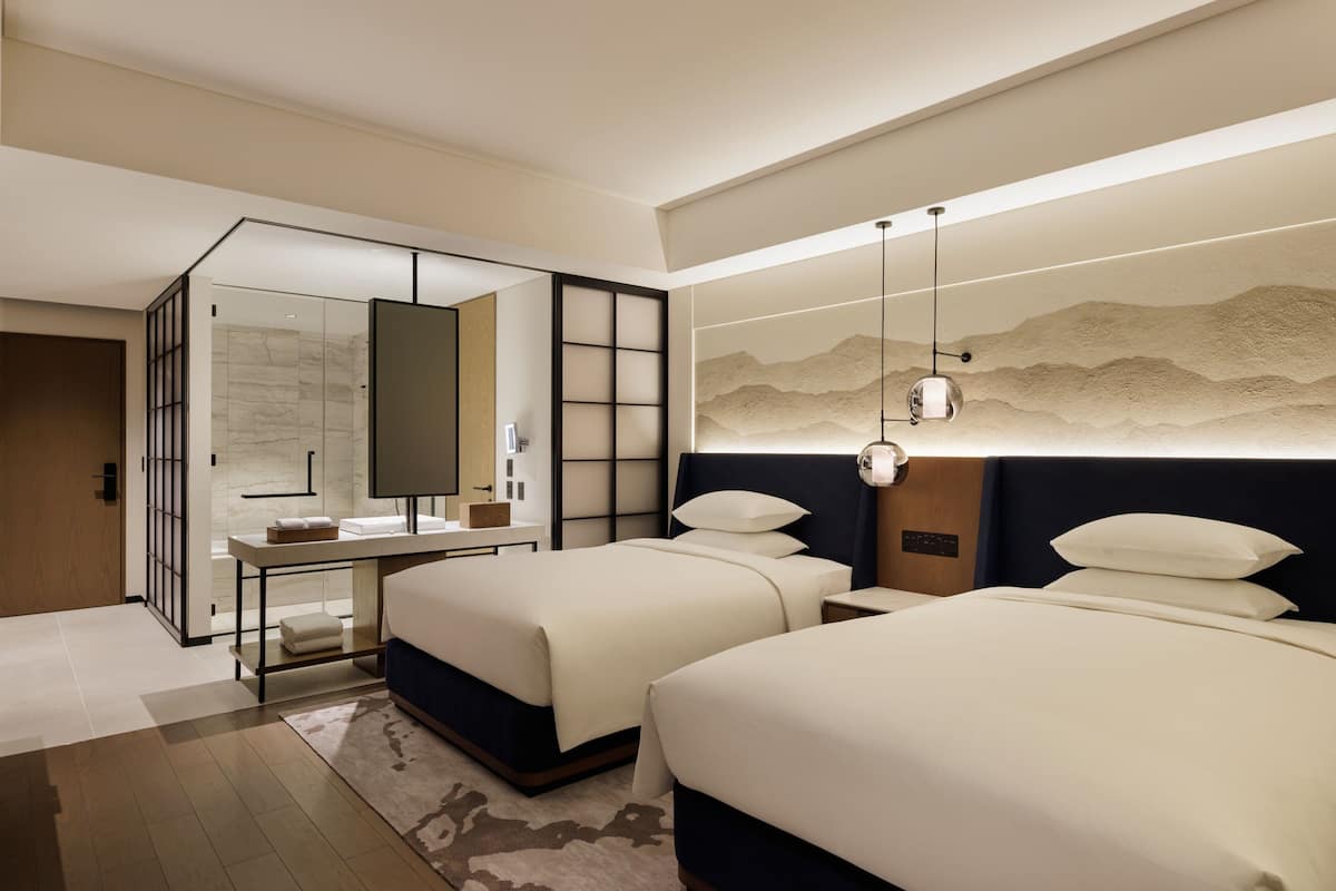 Ein modernes Hotelzimmer mit zwei Betten, einer Sitzecke mit Schreibtisch und einem großen Spiegel.