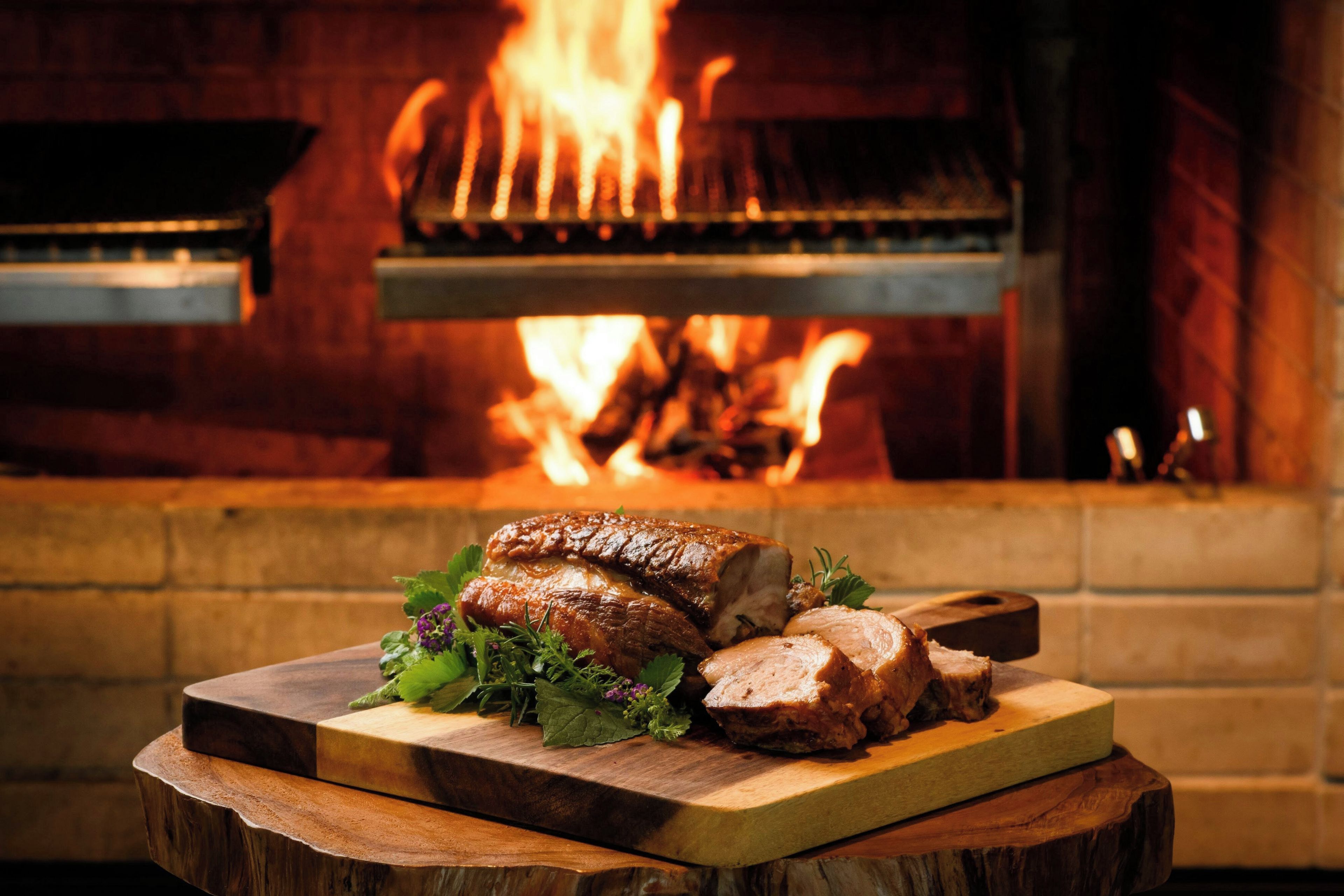 A roasted pork loin on a wooden board with a fire in the background.