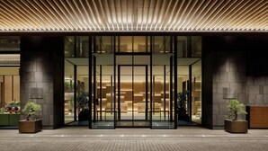 Entrada moderna de un hotel con puerta de vidrio, techo de listones de madera y un cartel que dice "Sheraton".