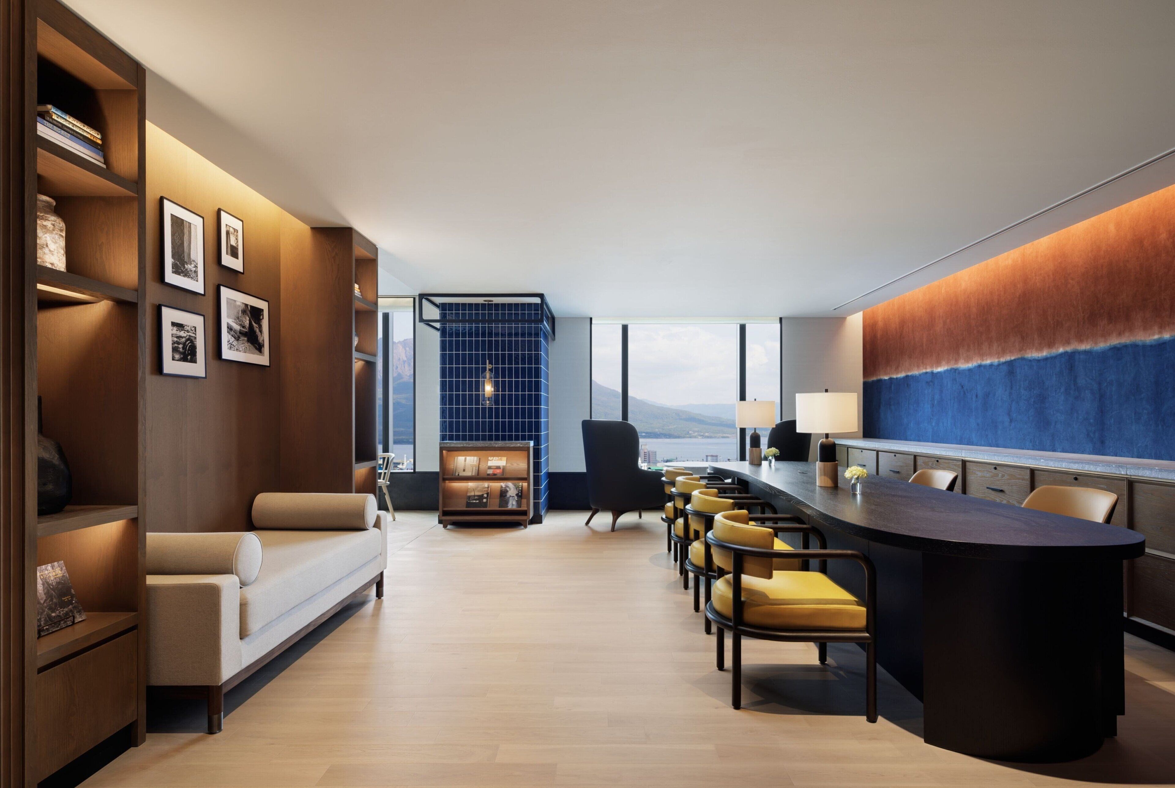 A modern hotel lobby with a long reception desk, seating area, and a bookshelf with framed photos.