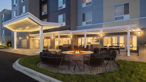 A hotel with a covered outdoor seating area featuring a fire pit, wicker chairs, and a pool.