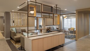 A modern living room with a sofa, a coffee table, and a TV. There is a wooden partition with a mirror and a hanging light fixture.