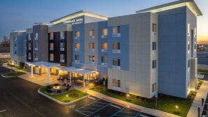 A modern hotel with a flat roof, a covered outdoor seating area, and a parking lot.