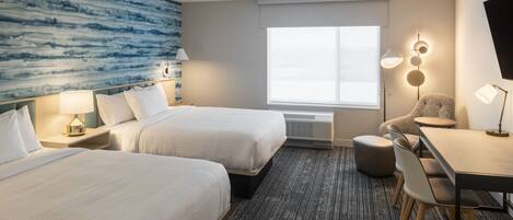 A hotel room with two beds, a desk, a chair, a large window, and a wall with a blue abstract design.