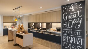 A modern kitchen with wooden cabinets, a central island, and a chalkboard sign saying "A Great Day Starts with Breakfast".
