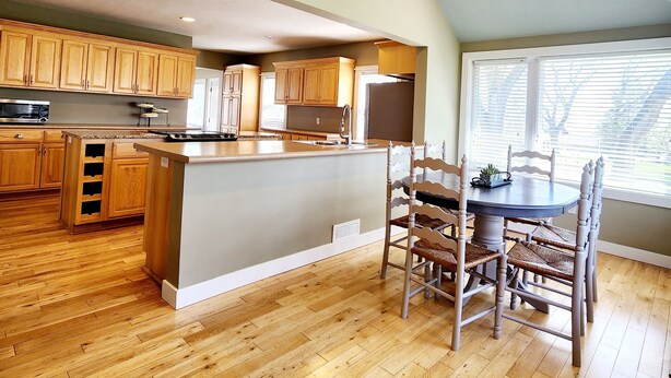 A spacious kitchen with wooden cabinets, a central island, and a dining area with chairs.