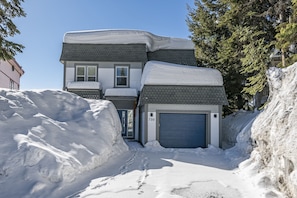A two-story house with a garage, surrounded by snow and trees.