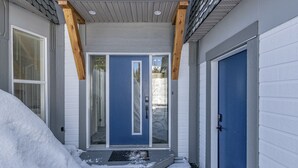 Une maison avec une porte d’entrée bleue, un porche en bois et un perron recouvert de neige.
