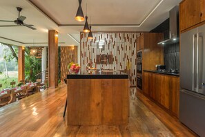 Enjoy meals in a well-equipped kitchen with a central island, dining area, and views of lush greenery.