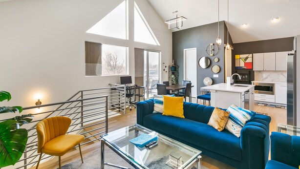 A modern living room with a blue sofa, yellow cushions, and a glass coffee table.