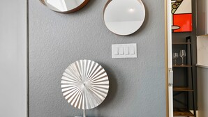 A wall with various mirrors and a decorative plate on a wooden stand.