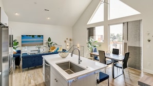 A modern kitchen with a large island, a dining area with a table and chairs, and a living area with a sofa and a painting of a beach.
