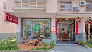 Un edificio con entrada de vidrio, un letrero y un pequeño espacio al aire libre con sillas y una estatua de perro.