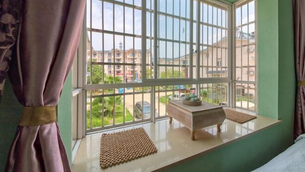 Una habitación con ventanas amplias, una cama, una mesita y vistas a edificios.