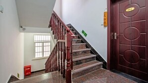 Una escalera con barandillas de madera y una puerta roja con placa numérica.
