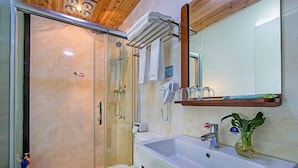 Un baño con cabina de ducha de vidrio, inodoro, lavabo con espejo y una planta pequeña.