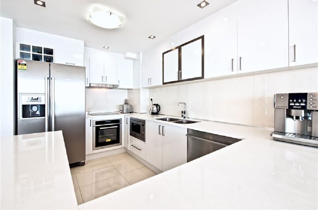 A modern kitchen with white cabinets, stainless steel appliances, and a built-in coffee machine.